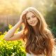 A-serene-sun-drenched-scene-of-a-woman-standing-in-a-lush-verdant-garden-surrounded-by A serene, sun-drenched scene of a woman standing in a lush, verdant garden, surrounded by thriving, vibrant plants. She gently brushes her voluminous, healthy hair, which flows down her shoulders in soft waves. The lighting is warm and diffused, creating a soothing, calming atmosphere. In the background, a wooden fence and a few scattered flower beds add to the tranquil, natural setting. The woman's expression is one of contentment and focus, as she mindfully attends to her hair care routine, embodying the concept of lifestyle changes for improved hair health.